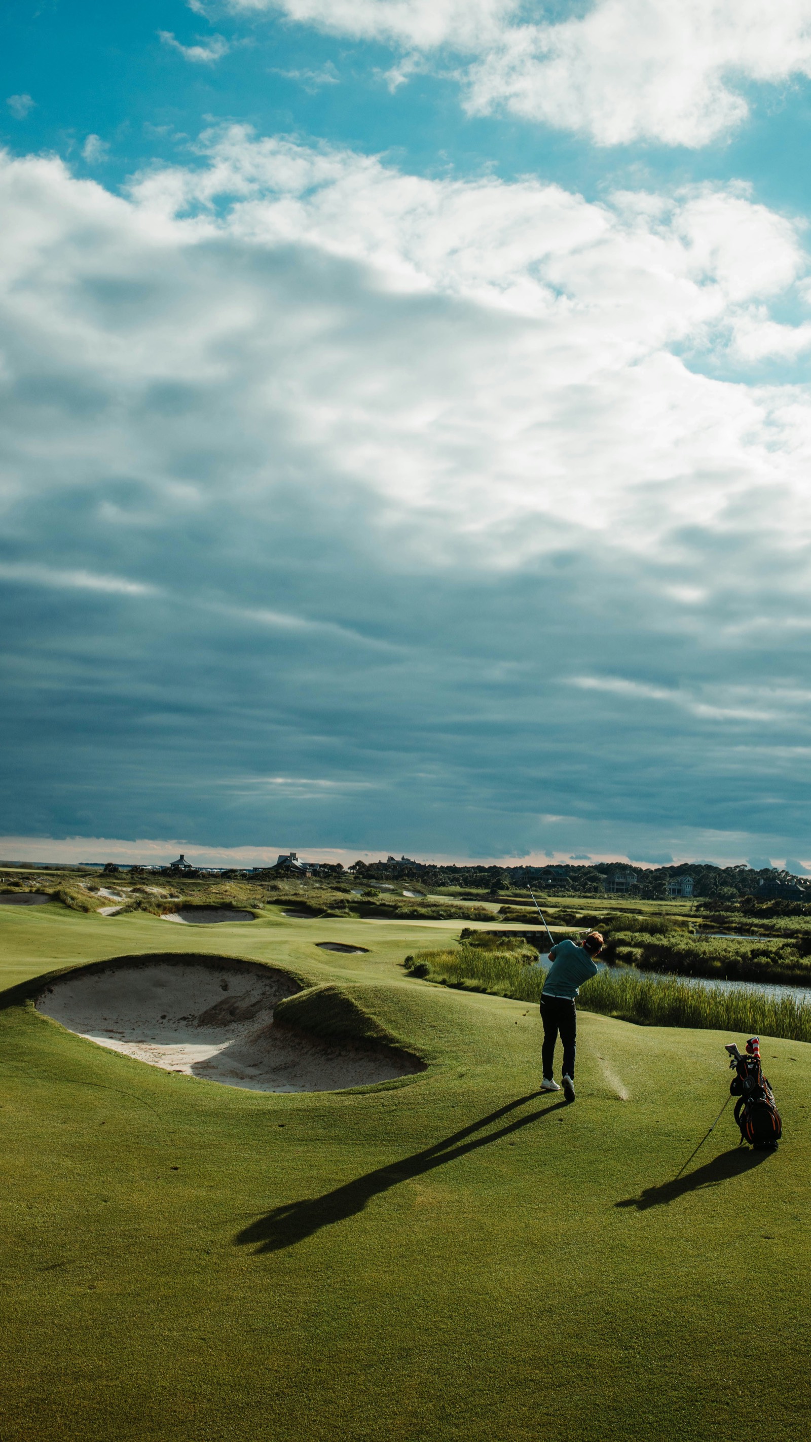 A golfer mid-swing on a links course under a dramatic cloudy sky.