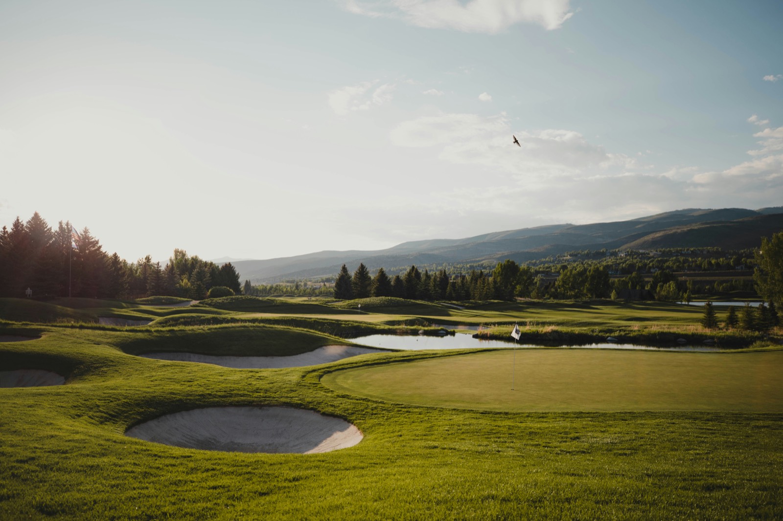 A golf green with bunkers and a pond, mountains in the distance at golden hour.